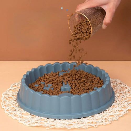 Blue anti-choking pet bowl with 3D obstacle maze design being filled with dry pet food, designed to slow down eating for safer, healthier meals.