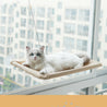 White cat lounging on a beige hanging cat window hammock by a city window