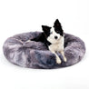 Black and white dog resting on a gray fluffy donut dog bed designed for calming and comfort for cats and dogs