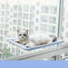 White cat resting on a blue hanging cat window hammock attached with suction cups on a window.