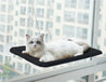 White cat lounging on black hanging cat window hammock attached with suction cups to a high-rise window for birdwatching and sunbathing.